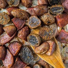 cooked sausages are on a wooden spoon next to some other food items that have been cut up