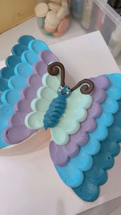 a blue and purple butterfly shaped cake sitting on top of a white table next to other items