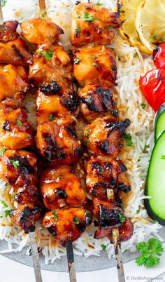 chicken skewers with rice, cucumber and tomatoes on a plate next to sliced cucumbers