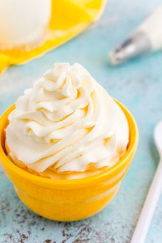 a yellow bowl filled with whipped cream on top of a blue table next to a spoon