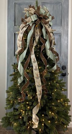 a decorated christmas tree in front of a blue door with lights and ribbon on it