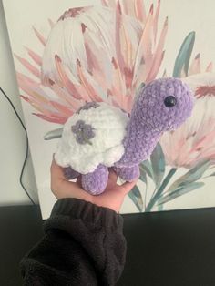 a hand holding a crocheted stuffed animal in front of a floral wallpaper