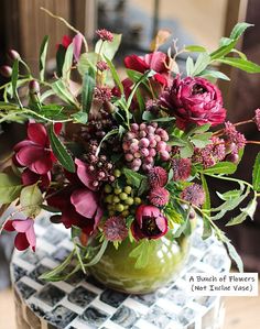 a green vase filled with lots of flowers on top of a checkered table cloth