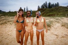 three women in bikinis standing on the beach with their faces covered by sun glasses