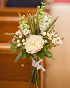 a bouquet of white flowers sitting on top of a wooden chair in front of a pew