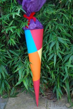 a colorful umbrella sitting on top of a lush green field next to tall grass and bushes