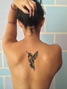 a woman with a hummingbird tattoo on her back shoulder and behind her is a brick wall