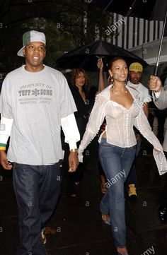 a man and woman walking in the rain under an umbrella with other people behind them