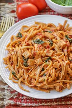 a white plate topped with pasta next to a bowl of tomatoes and spinach leaves