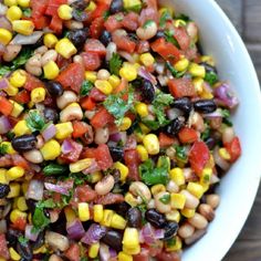 a white bowl filled with corn, black eyed peas and cilantro peppers on top of a wooden table