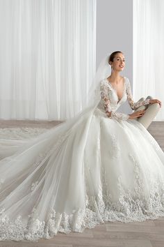 a woman sitting on the floor wearing a wedding dress with long sleeves and a veil