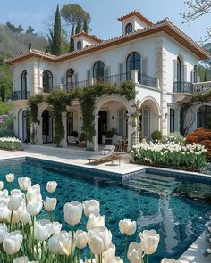 a large house with a pool in front of it and lots of white flowers around the pool