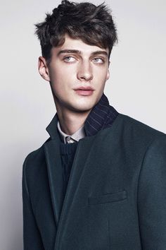 a young man in a green coat posing for the camera with his eyes wide open