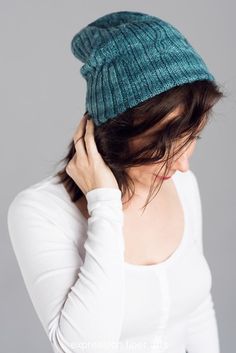 a woman wearing a green knitted beanie with her hands on her head and looking down