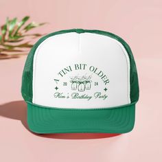 a green and white trucker hat sitting on top of a pink surface