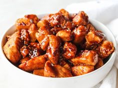 a white bowl filled with chicken sitting on top of a table next to a napkin