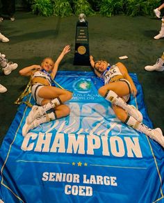 two cheerleaders laying on the ground in front of a trophy