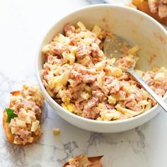 a white bowl filled with tuna salad next to some bread