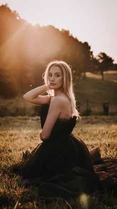 a woman is sitting in the grass with her hands on her head and looking at the camera