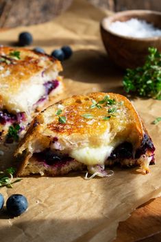 two grilled cheese sandwiches with blueberries and parsley on a wooden cutting board