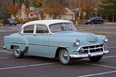 an old blue and white car parked in a parking lot