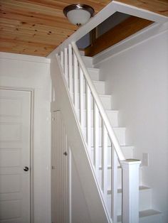 an empty room with white stairs and wooden ceiling