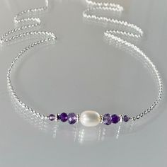 Genuine, premium-quality, purple amethyst gemstone and freshwater pearl bar necklace in sterling silver. Modern and minimal, this necklace is hand-crafted with genuine, faceted, graduated, light and dark amethyst gemstones and a single, creamy-white, oval white freshwater pearl.  These are artfully fashioned into a bar, wire-wrapped onto a dainty but sturdy sterling chain.  A sterling silver oval lobster clasp secures this necklace. Amethyst is the birthstone for February and pearl June. Details: necklace length: please choose at check-out genuine faceted amethyst:  4, 3 and 2 mm genuine white freshwater pearl: approx. 4x6 mm sterling silver chain, saucer bead, daisy bead and clasp Thanks for visiting ! Back to my shop for more jewelry options: www.etsy.com/shop/krisatdesigns. Purple Pearl Necklace, London Blue Topaz Necklace, Green Onyx Necklace, Pearl Bar Necklace, London Blue Topaz Earrings, December Birthstone Necklace, Blue Topaz Necklace, Silver Bead Necklace, Purple Pearl