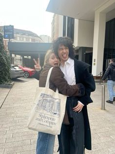 a man and woman hugging each other while standing on the sidewalk in front of a building