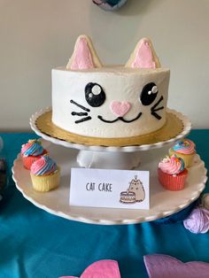 a cat cake sitting on top of a plate next to cupcakes