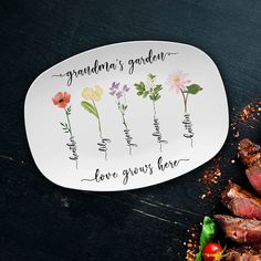 a white plate with flowers on it next to some steaks and vegetables in the background