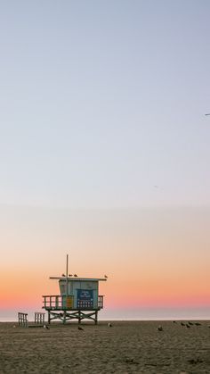 a lifeguard station on the beach with birds flying in the background at sunset or dawn