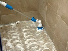 a tile shower is being cleaned with a blue and white sprayer on the floor