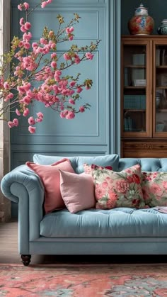 a blue couch sitting in front of a vase filled with pink flowers