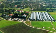 an aerial view of a parking lot in the middle of a green field with houses and trees