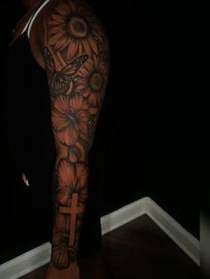 a person with a cross and sunflowers tattoo on their arm is standing in a dark room