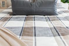 a bed with a checkered comforter and pillow on it, next to a potted plant