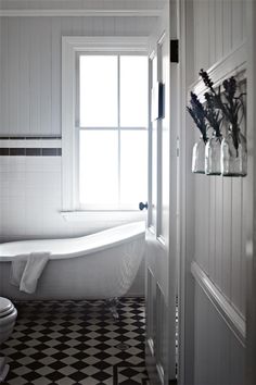 a white bathtub sitting next to a toilet in a bathroom on top of a black and white checkered floor