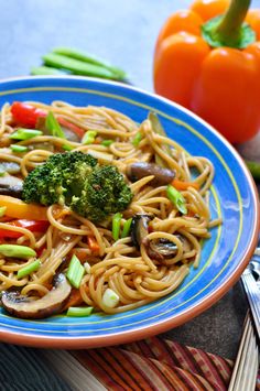 a blue and orange plate with noodles, broccoli, mushrooms and carrots