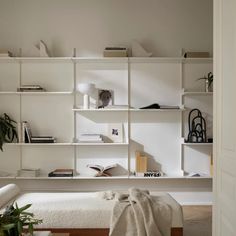 a white book shelf filled with books next to a bed and potted plant on top of it