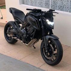 a black motorcycle parked in front of a building next to a sidewalk with a window