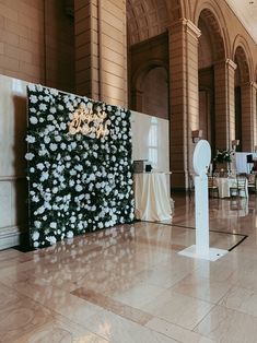 a large room with tables, chairs and white flowers on the wall behind an art piece