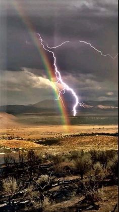 a rainbow appears to be in the middle of a desert with storm clouds and lightning