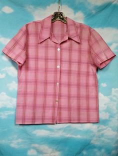 a pink plaid shirt hanging on a blue and white wall with clouds in the background