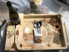 a wooden tray with utensils and napkins on it next to a bottle of wine