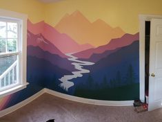 a room with mountains painted on the wall and a cat laying on the floor in front of it