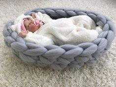 a baby doll is laying in a blue rope basket on the floor next to a white rug