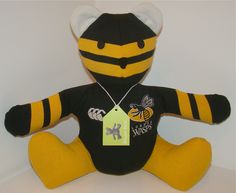 a yellow and black stuffed animal with a tag on it's chest, sitting in front of a white wall