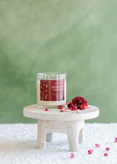 a candle sitting on top of a white table next to pink flowers and petals in front of a green wall