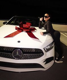 a woman sitting on the hood of a white car with a red ribbon around it