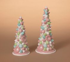 two small christmas trees are decorated with pastel colors and flowers on pink bases, against a brown background